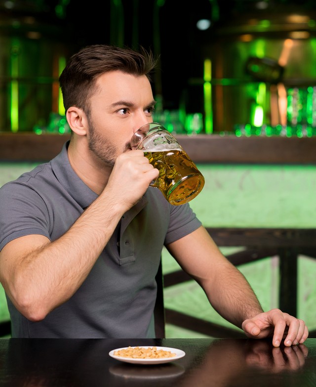 Drinking fresh beer. Thoughtful young man drinking beer and looking away while sitting in bar